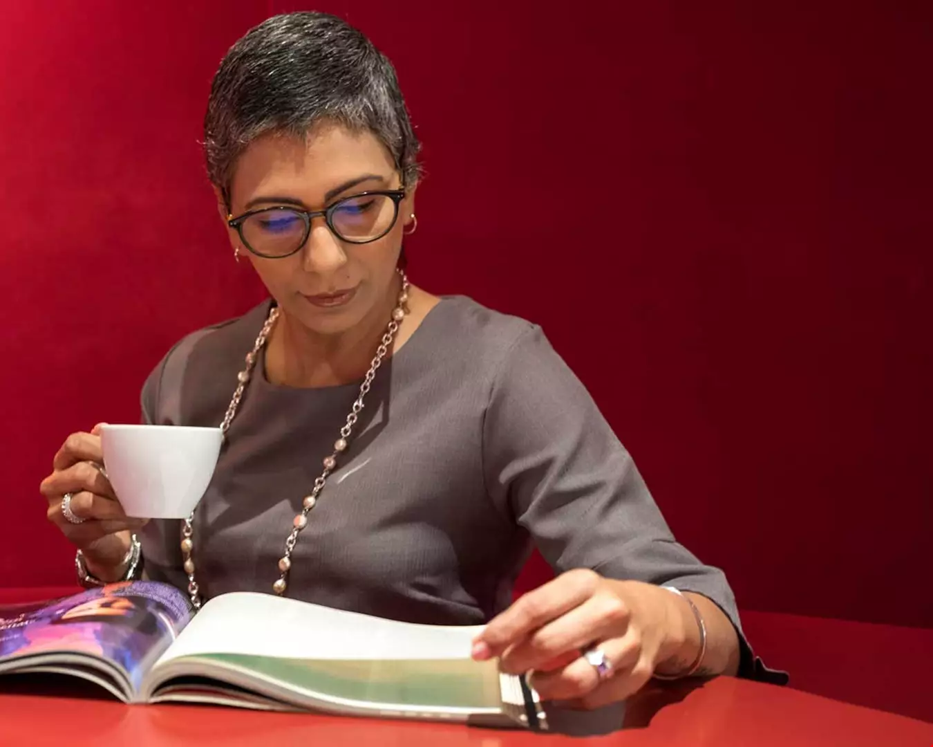 Kvinna i medelåldern, grått kort hår, kaffekopp i handen, läser i en pärm