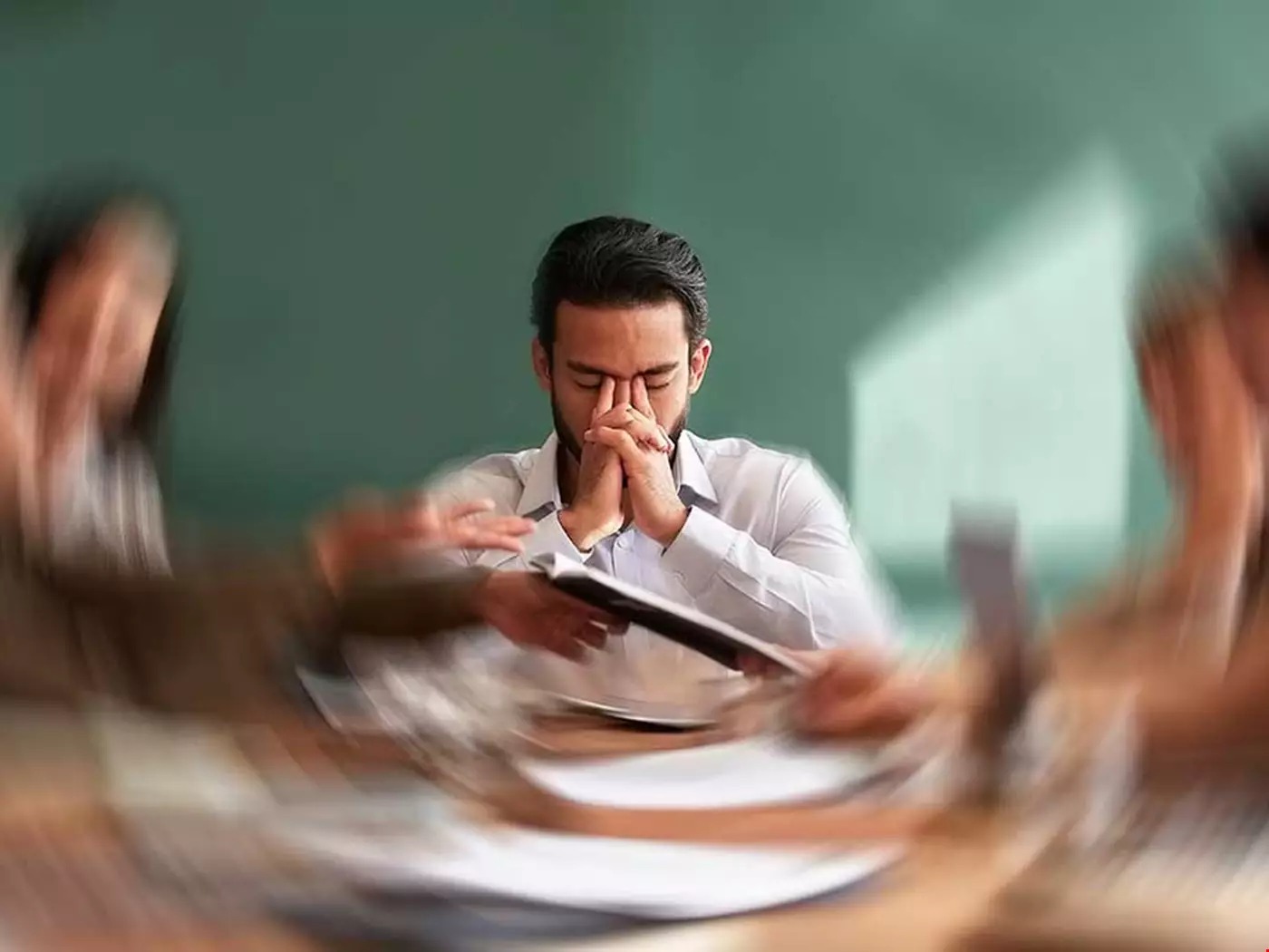 En man i kontorsmiljö ser ut att få tunnelseende av stress, kollegor ute i periferin i bilden flimrar och arbetsuppgifterna ser ut att hopa sig på ett negativt sätt. Mannen ser förtvivlad ut och gömmer sitt ansikte i händerna.