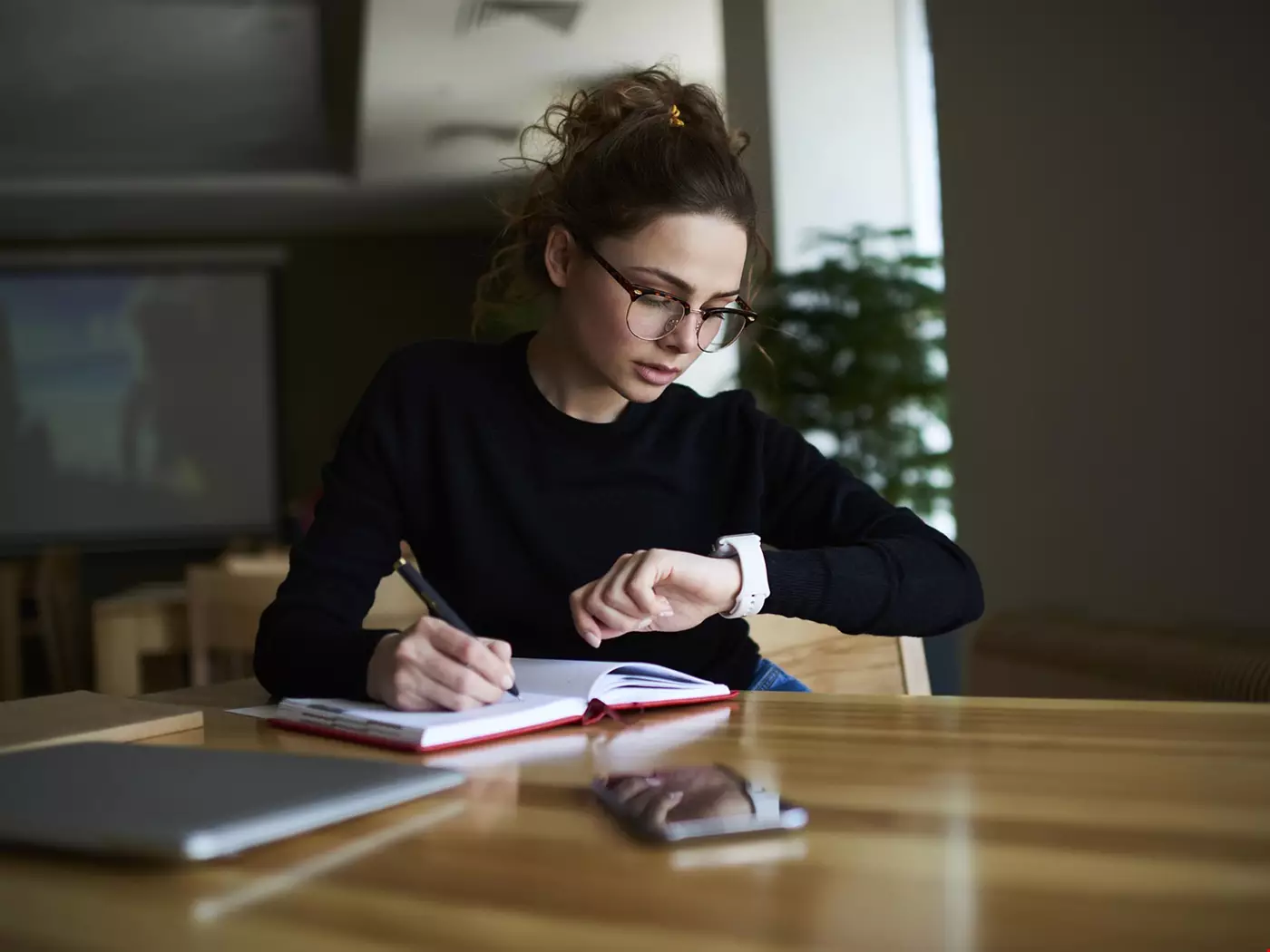 Ung kvinna student skriver i en almanacka tittar på klockan