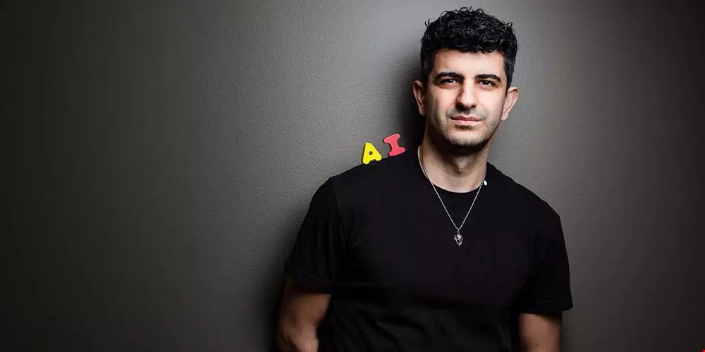 Medelålders man lutar sig mot mörk vägg, svart t-shirt, balanserar ett rött A och ett gult I på axeln, bildar förkortningen AI, Arash Gilan porträtt Akavia Aspekt