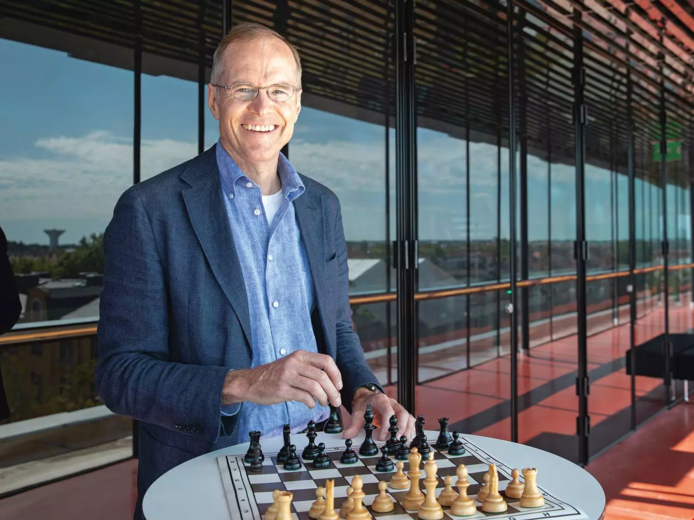 Medelålders man med glasögon, blå skjorta och mörkblå kavaj, utomhus framför en glasvägg